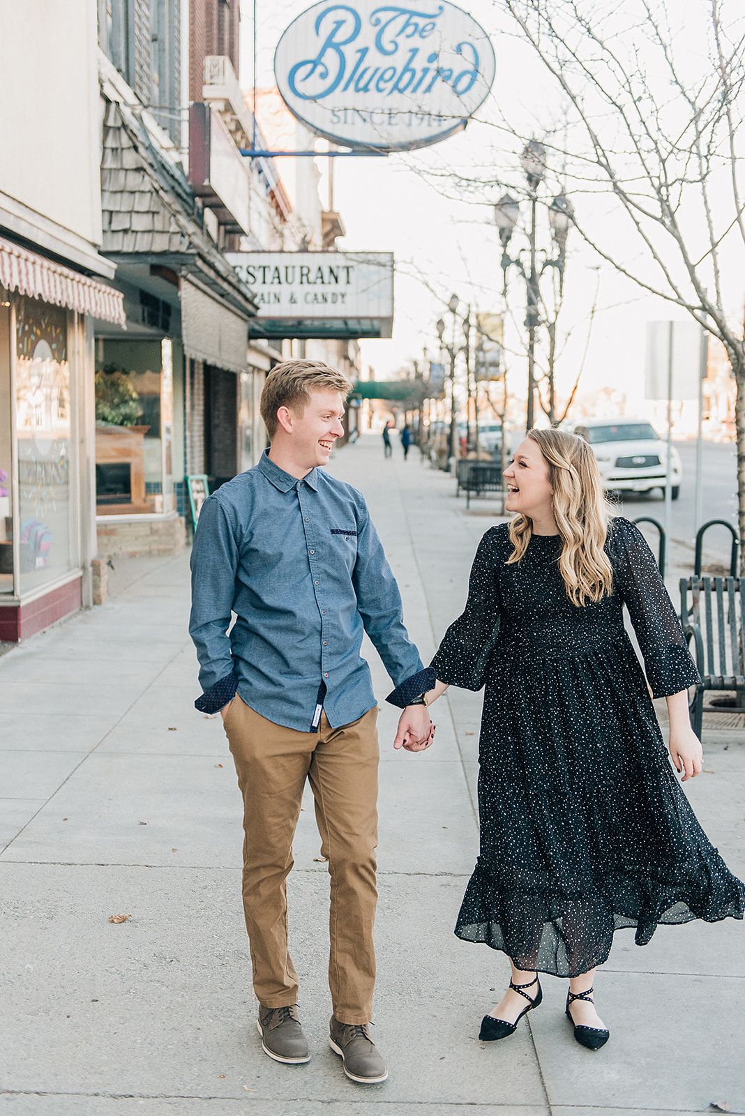 Couple walking hand in hand on sidewalk past Bluebird restaurant sign in downtown area.