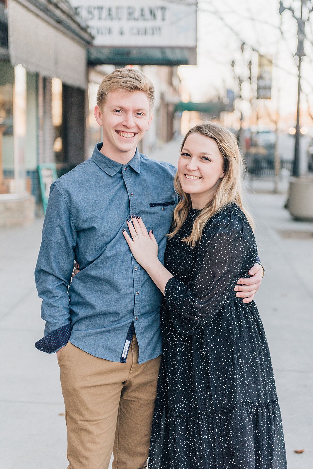 Couple posing together outside restaurant, dressed in blue shirt and polka dot dress.