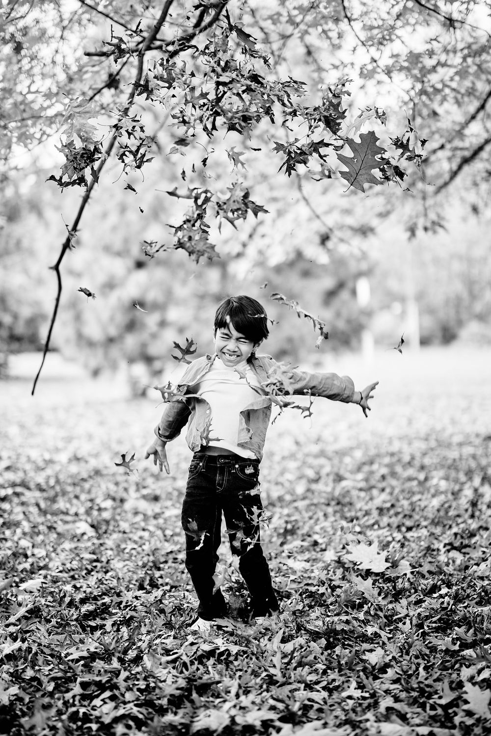 Black and white sequence of a child playing and exploring in fallen autumn leaves under a tree.