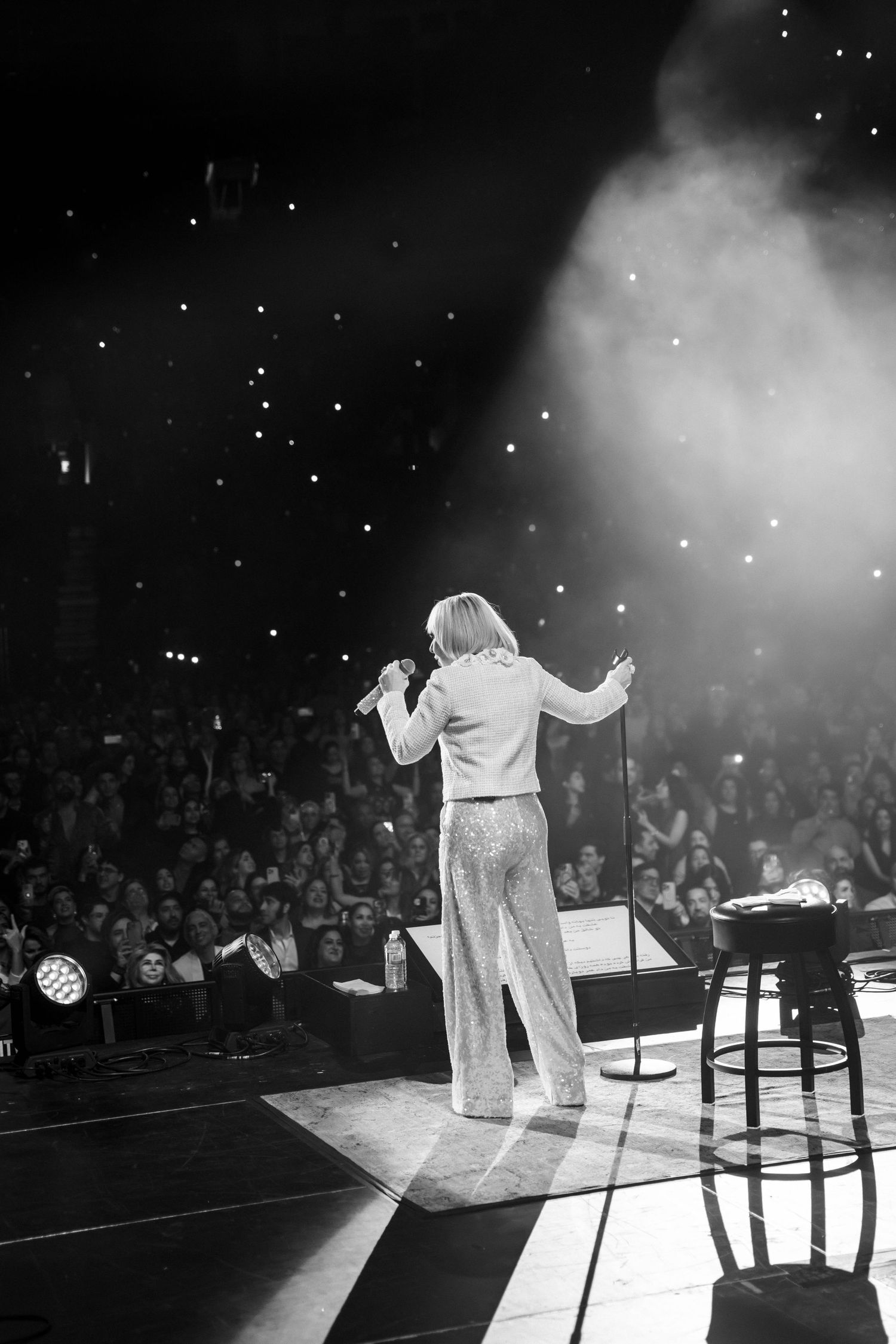 Performer on stage in dramatic black and white photo with spotlights and smoke effects.