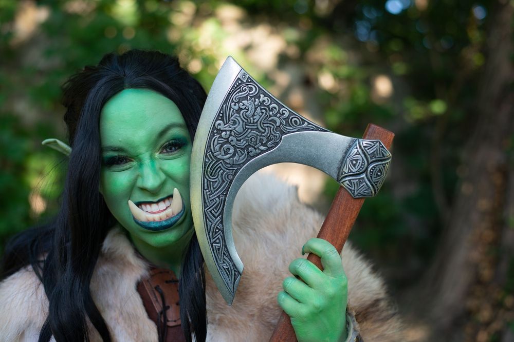 Orc character with green face paint and dark hair brandishes ornate battle axe against forest backdrop.