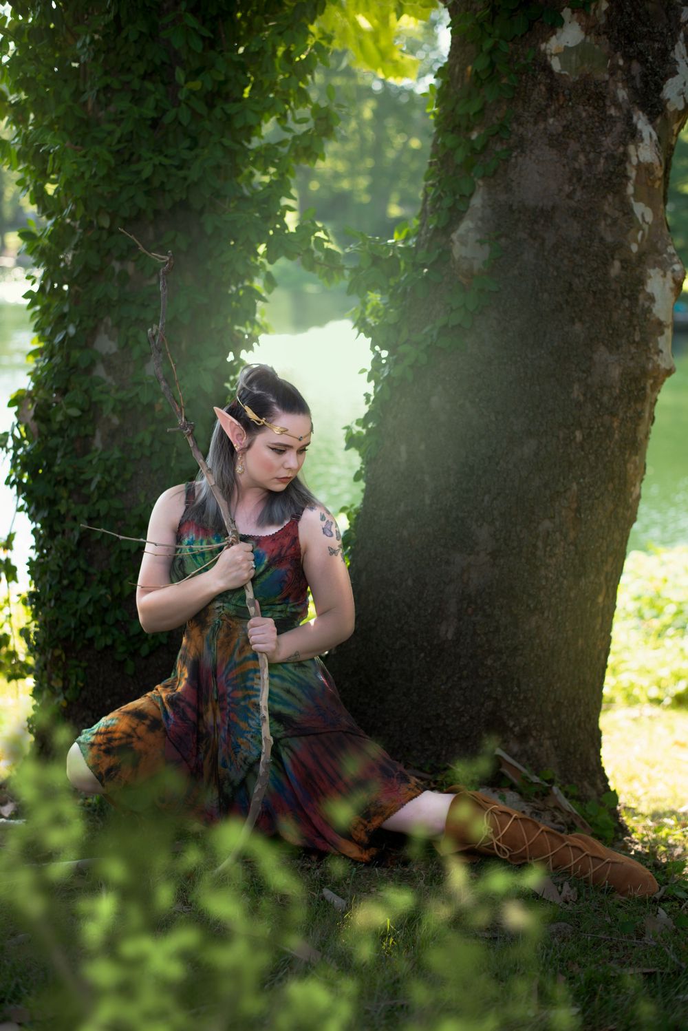 Fantasy-inspired portrait of person in colorful dress by mossy tree.