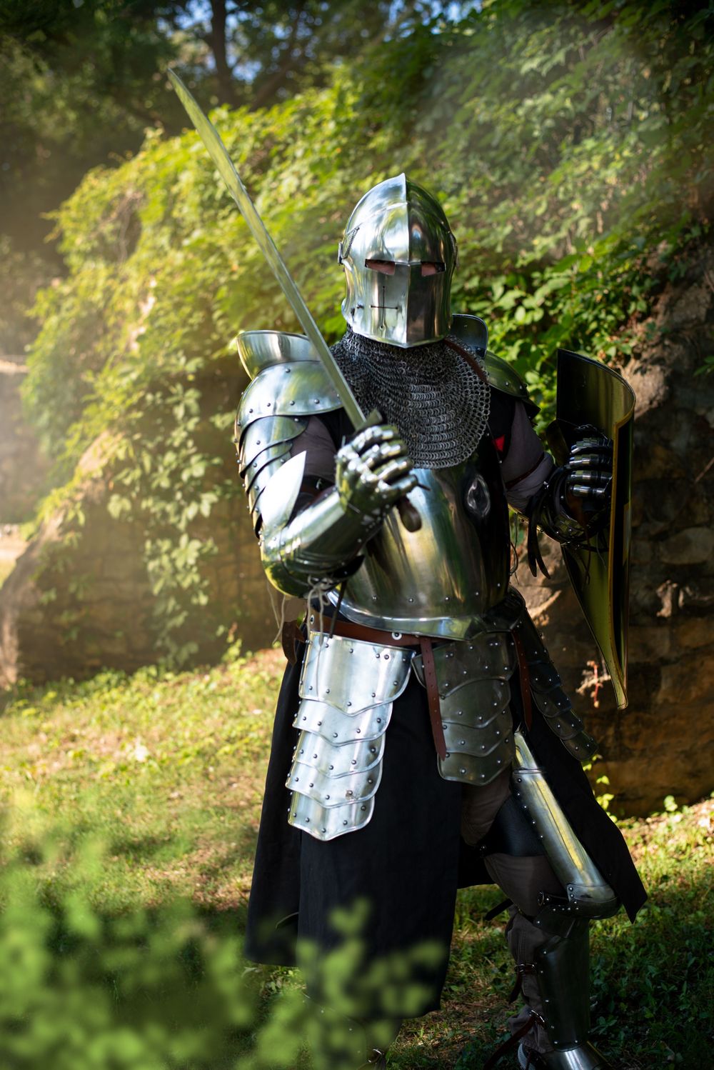 Knight in full plate armor and chainmail stands guard in dappled forest light.