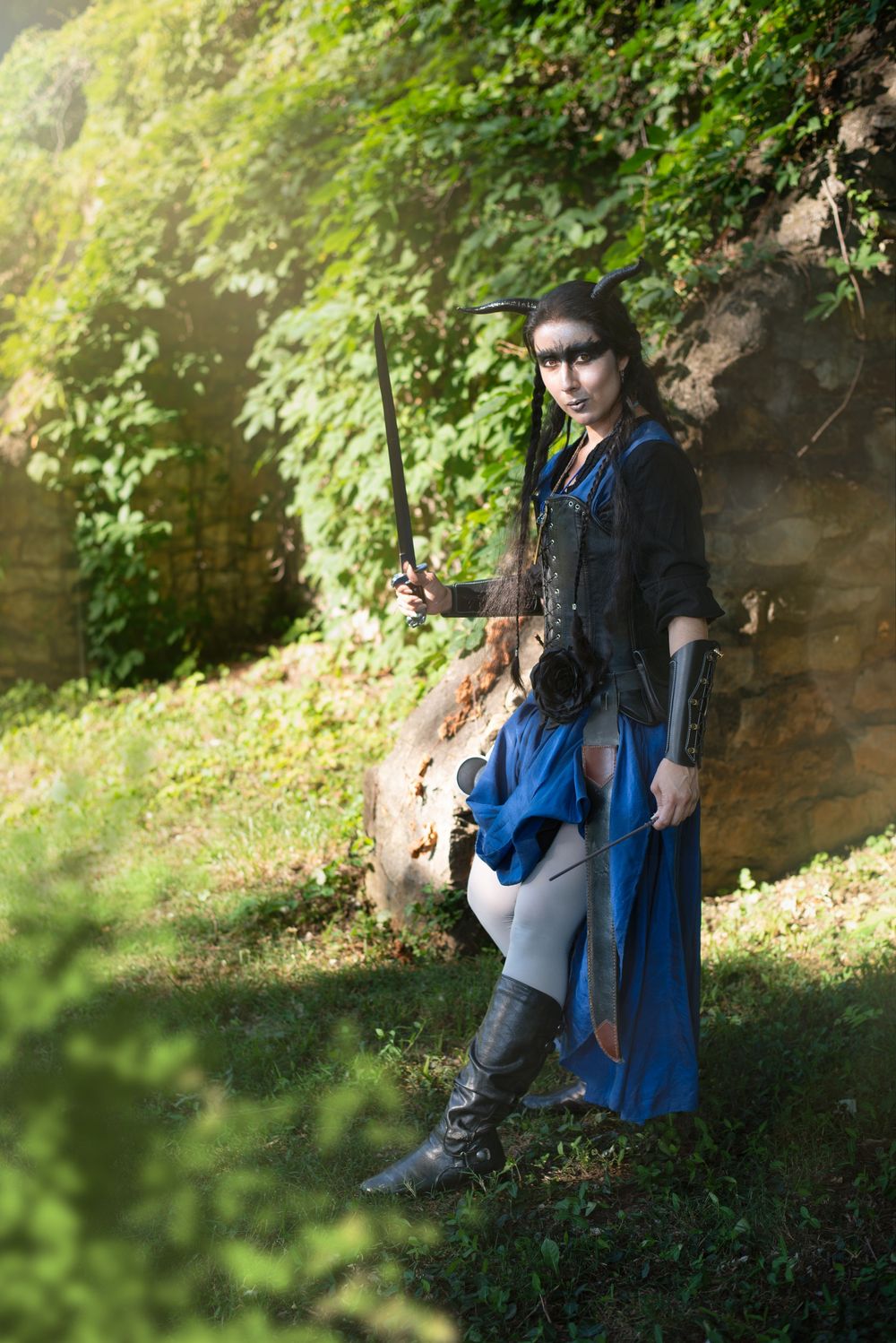 Medieval-dressed adventurer rests against stone wall in a forested setting.