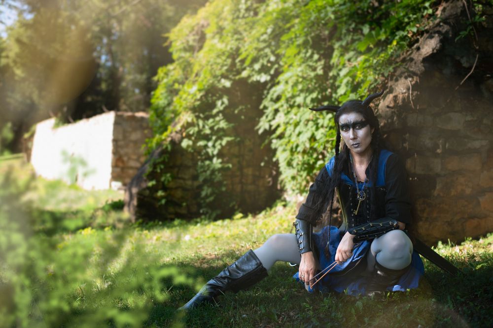 A person in a black outfit sits on a fallen tree trunk in a wooded forest setting.