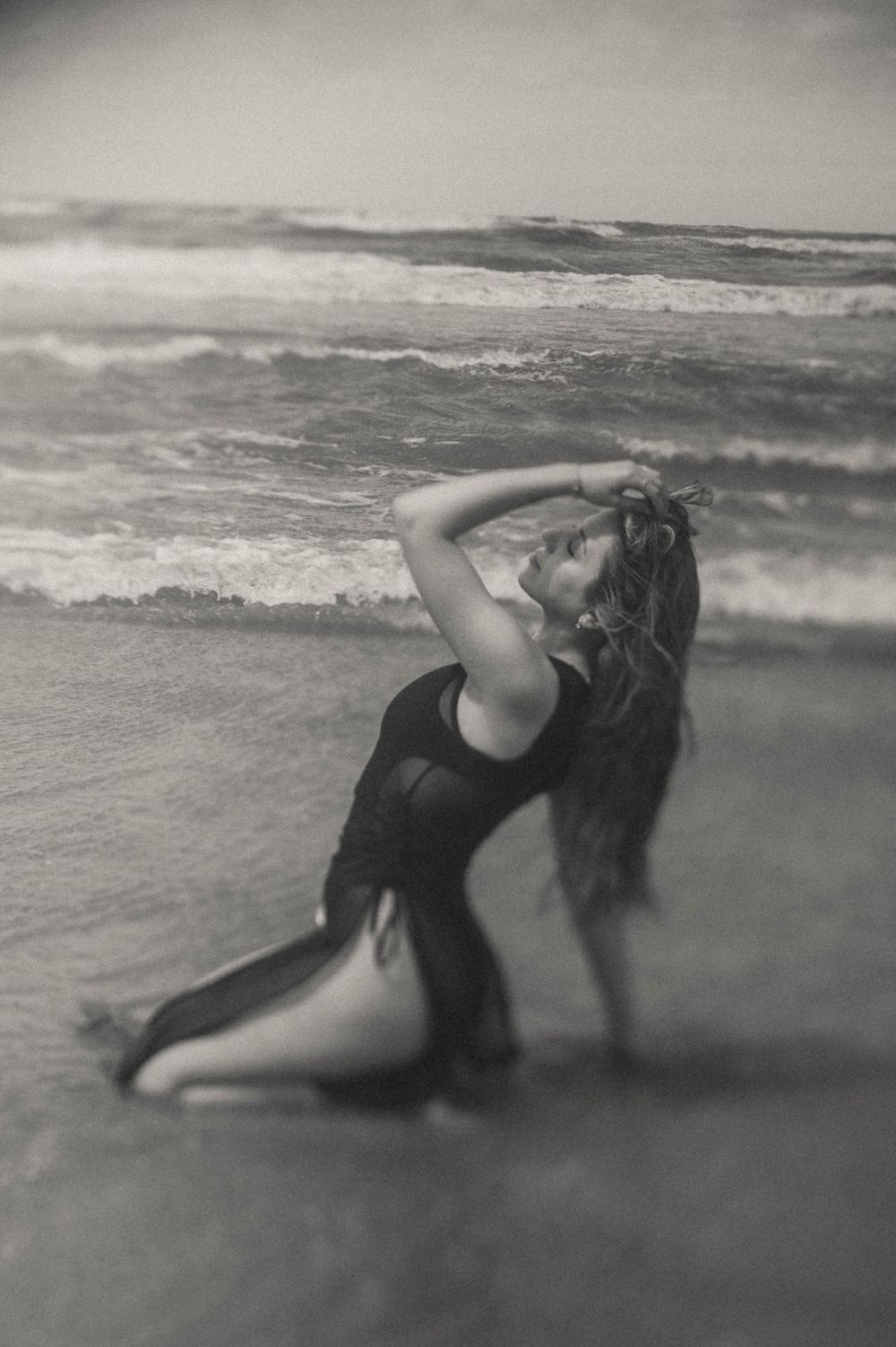 Artistic black and white photo of person posing in waves at the beach.