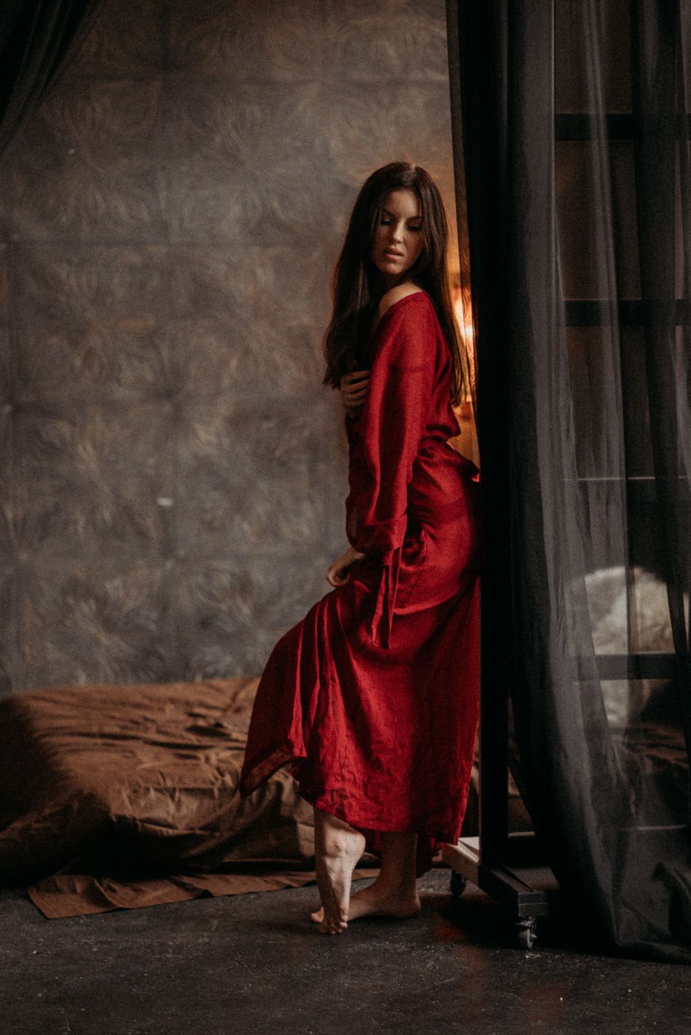 Figure in a striking red dress poses dramatically against textured walls in moody lighting.