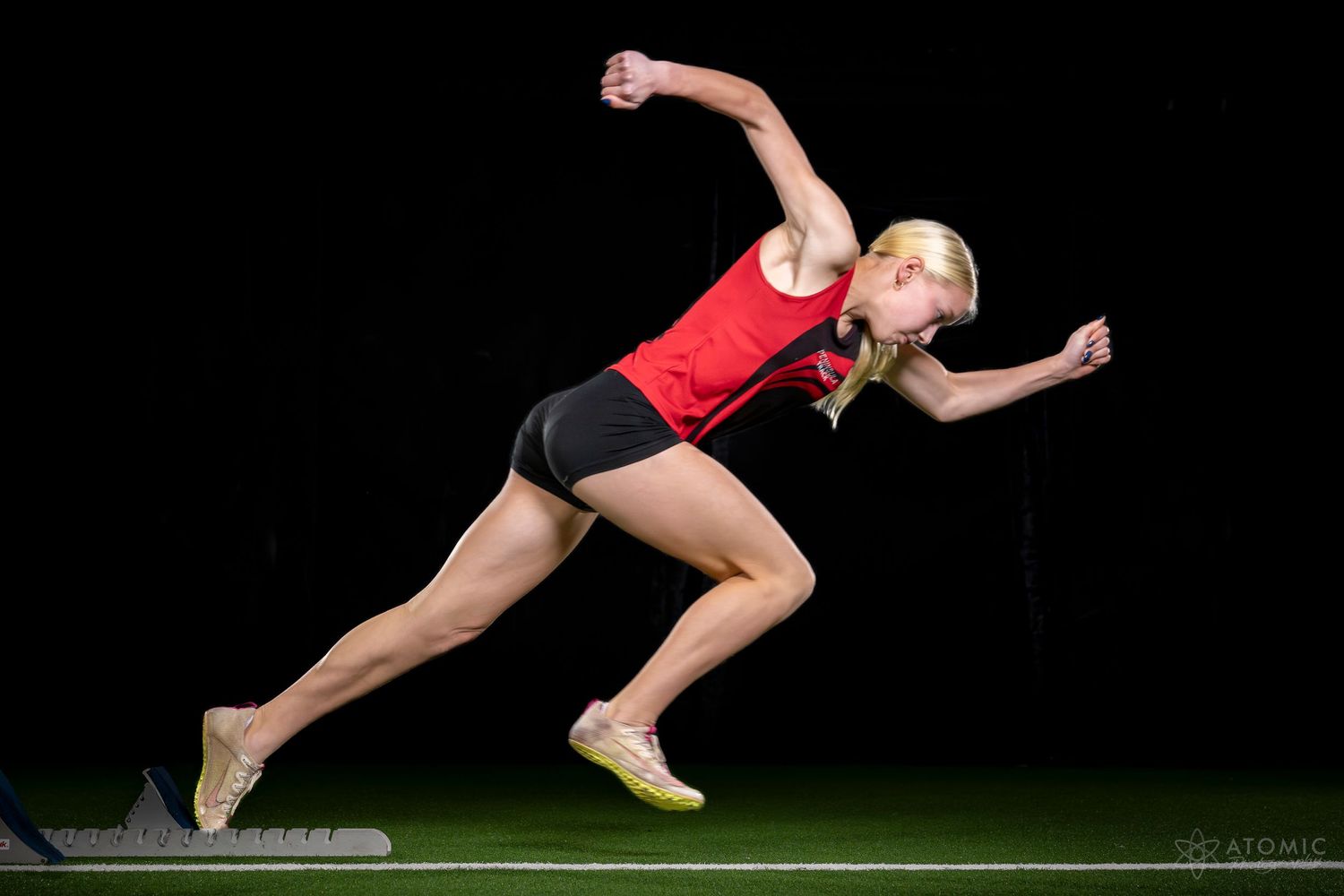 A studio photo of a young female sprinter bursting out of the starting blocks.