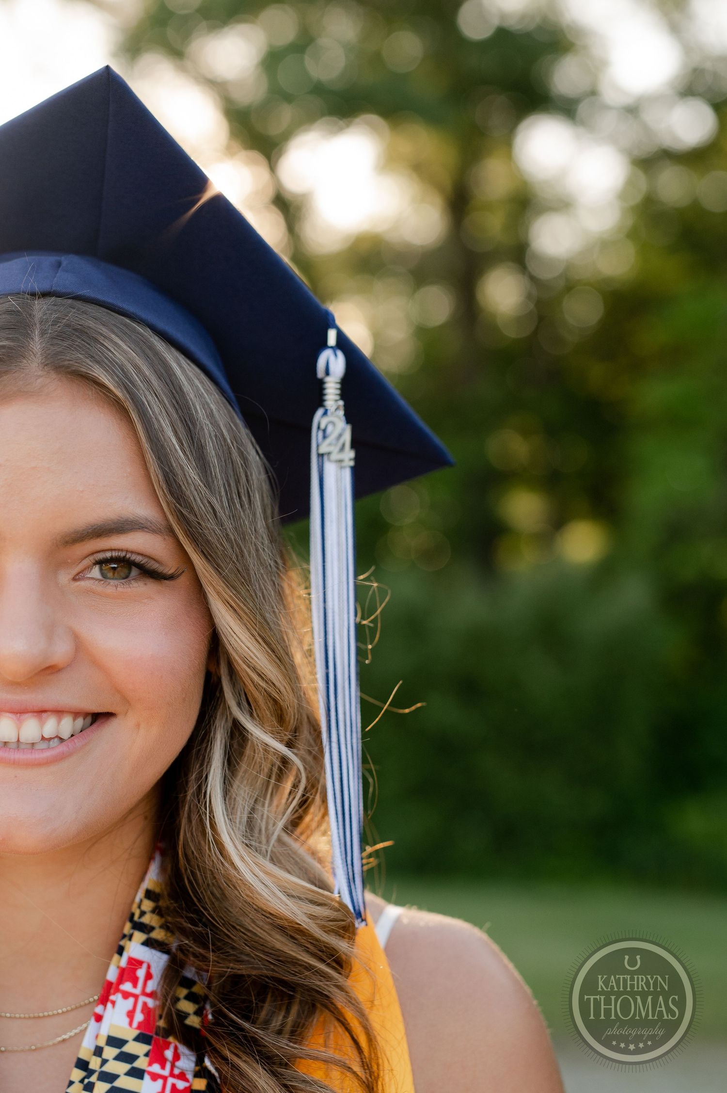 Graduate in navy cap and gown with white tassel poses outdoors during golden hour.