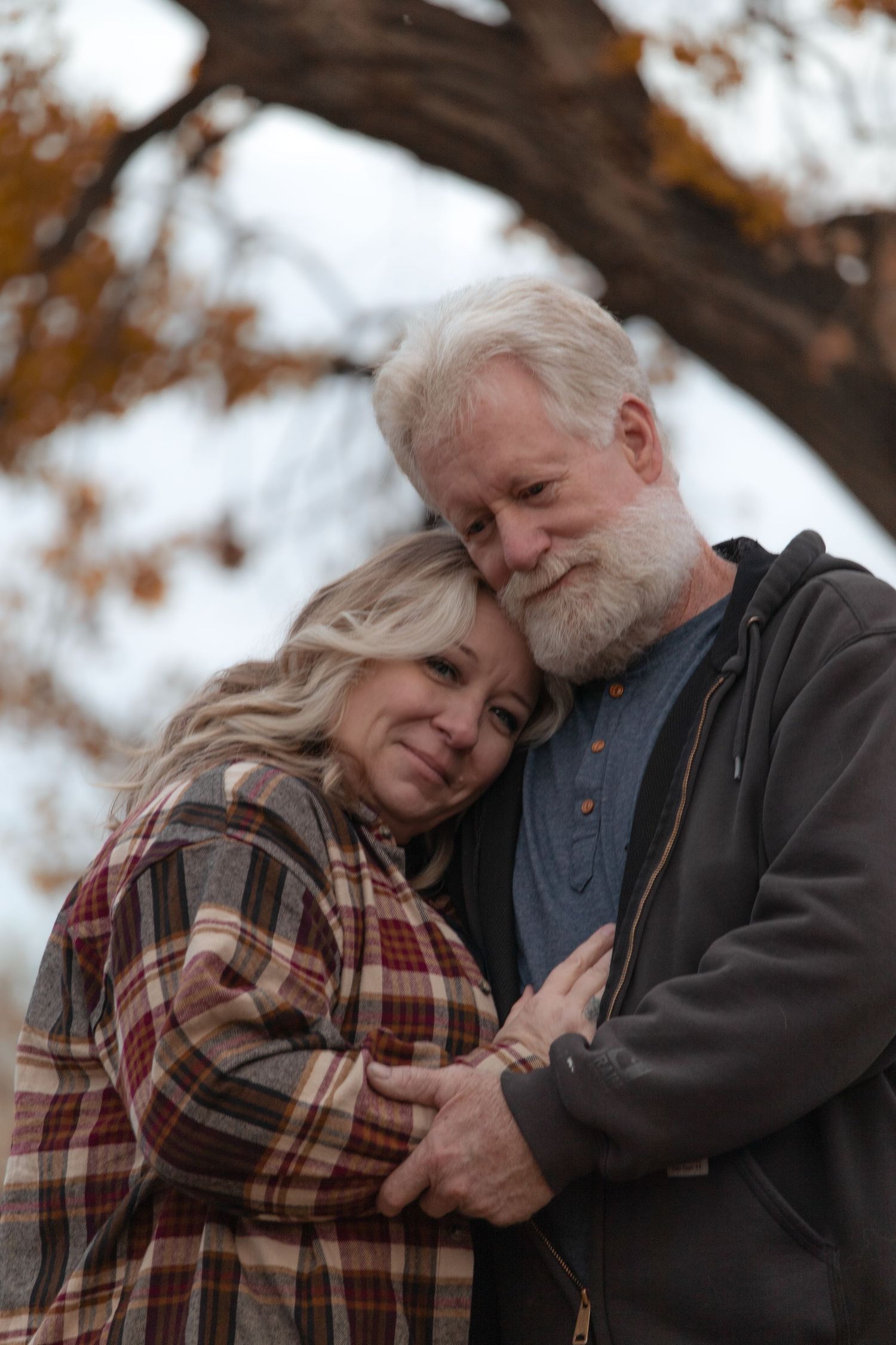 Sweet moment between older couple embracing under autumn leaves during a love story session in Tri-Cities WA