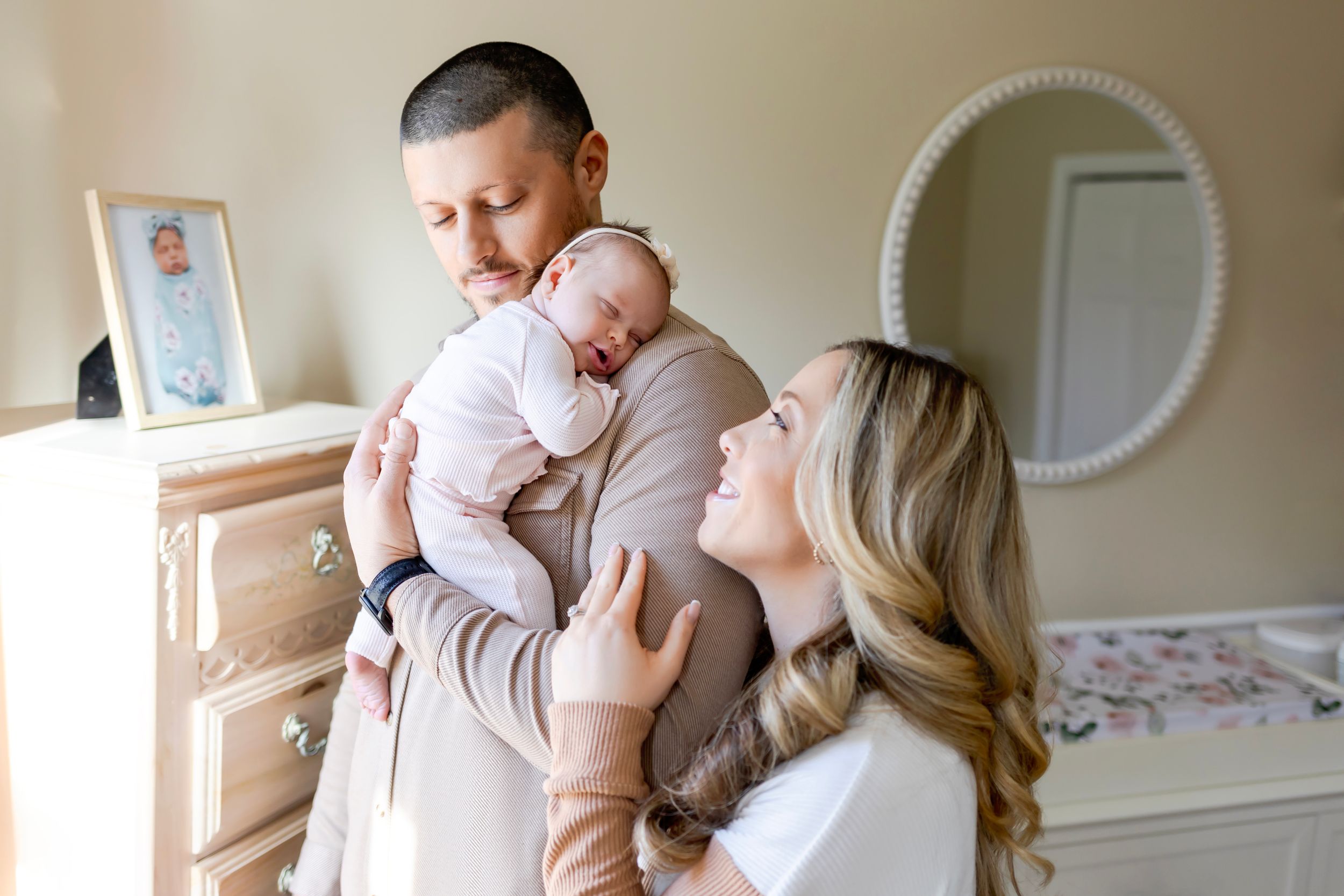 Mom and Dad in a nursery tenderly holding their sleeping baby. NJ Newborn Photographer in home session.