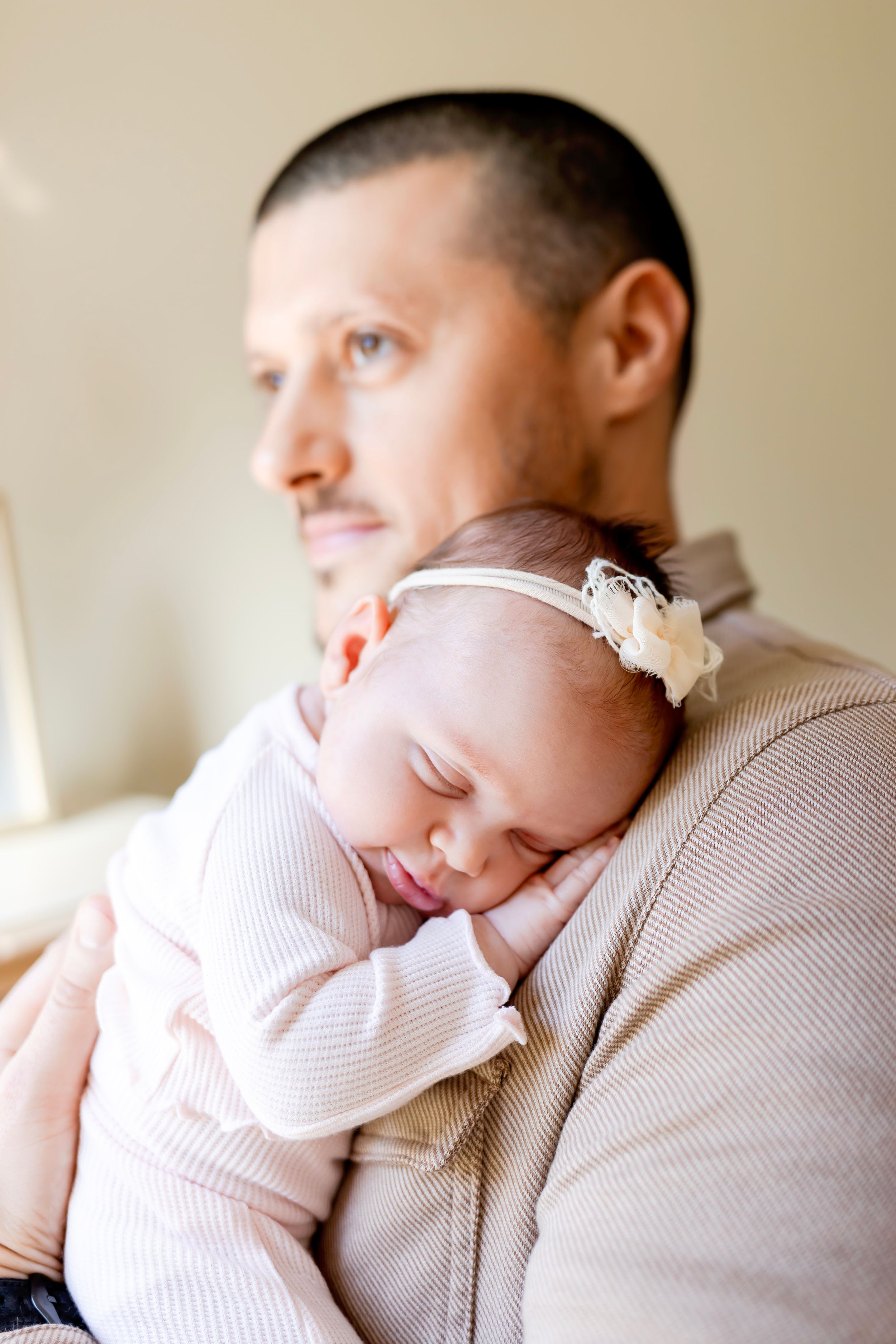 A sleeping baby in a white outfit and headband rests on DAD'S chest. NJ Newborn Photographer in home session.