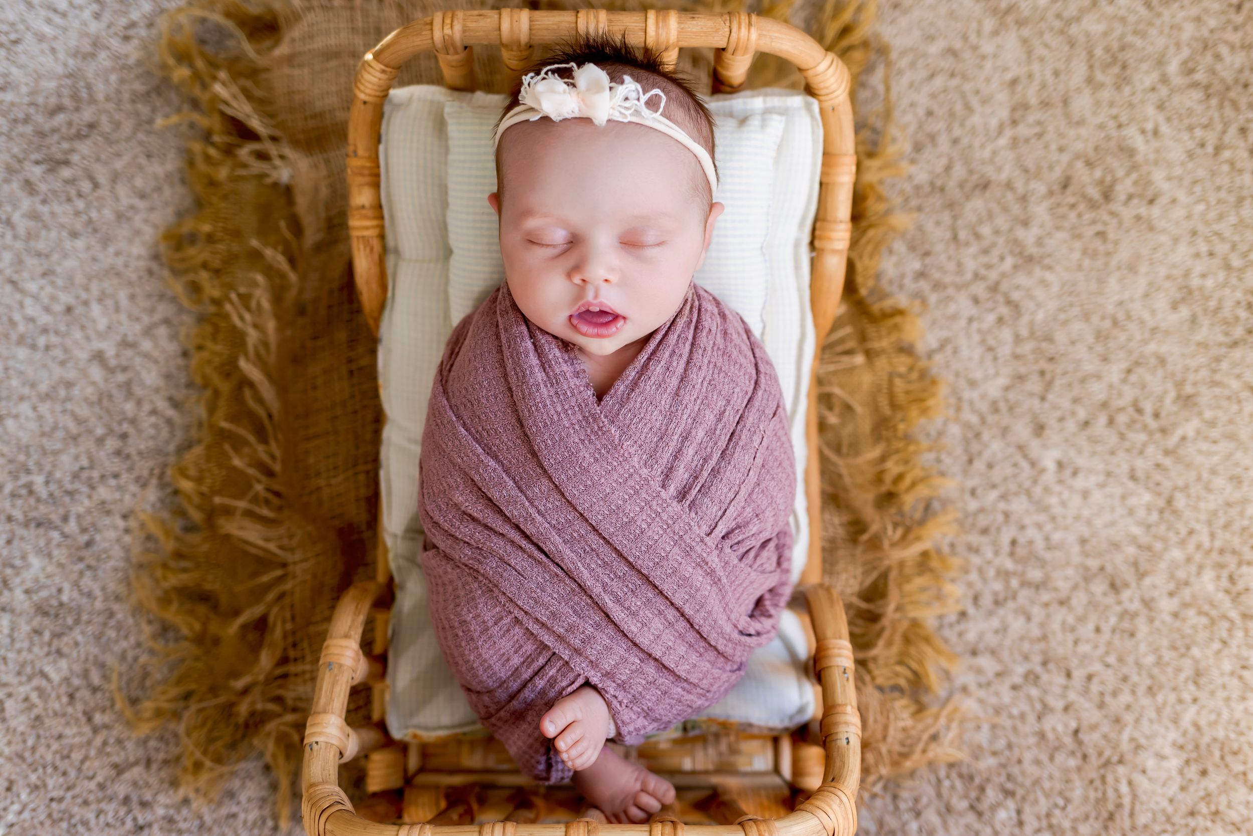 Sleeping newborn wrapped in mauve swaddle blanket laying in wooden basket with fur trim. NJ Newborn Photographer in home session.