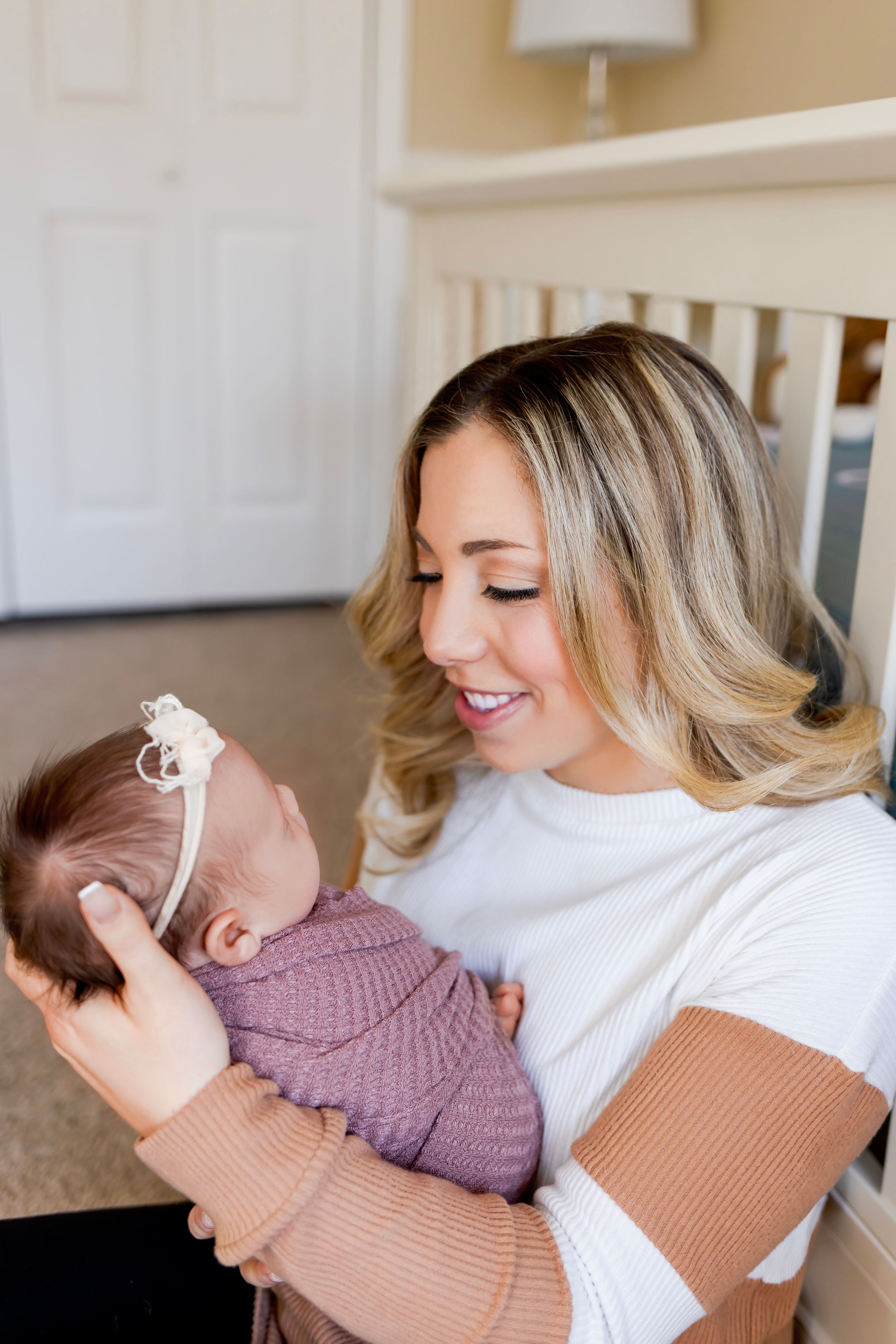 Mom holds and lovingly gazes at a sleeping baby wearing a purple knit sweater. NJ Newborn Photographer in home session