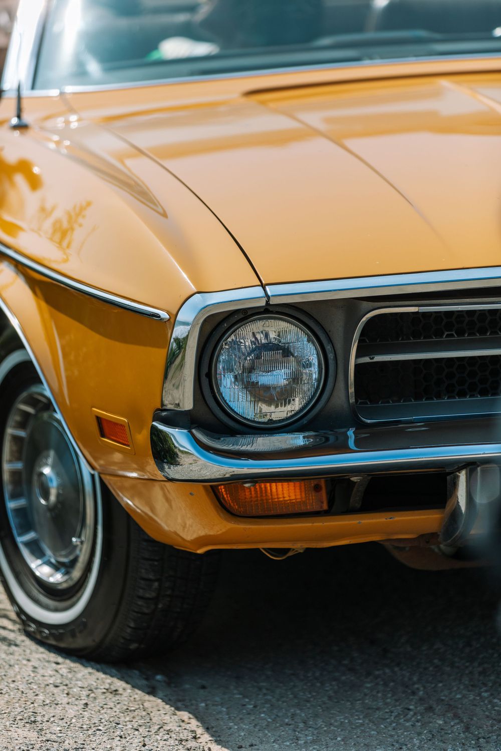 Close-up view of a classic yellow Mustang's front end showing its round headlight and chrome trim details.
