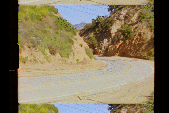 A winding coastal mountain road curves around rugged cliffs with blue ocean visible in the distance.