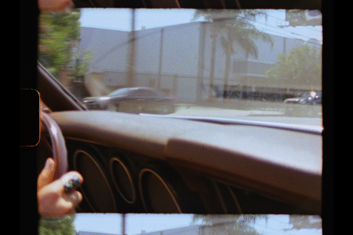 View from inside a vintage car showing brown leather dashboard and palm trees visible through windshield.