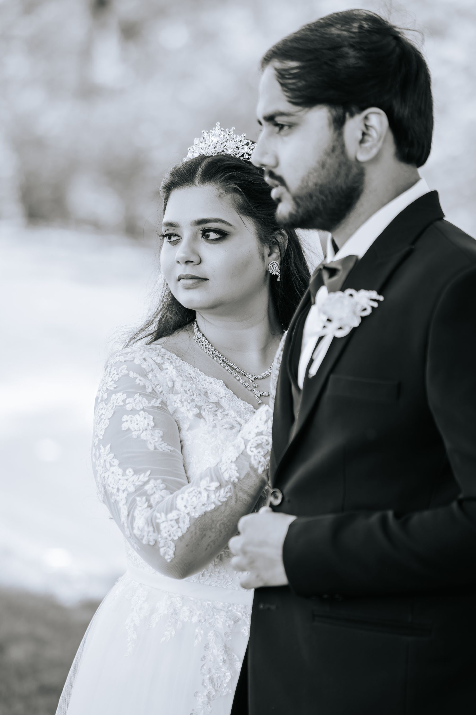 Black and white photo of a bride in lace gown and tiara with groom in suit at their wedding.