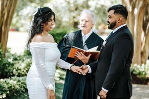 Couple exchanging vows outdoors with officiant holding book during elegant wedding ceremony.