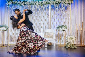 Couple sharing romantic first dance at elegant wedding reception with floral backdrop and gold decor.