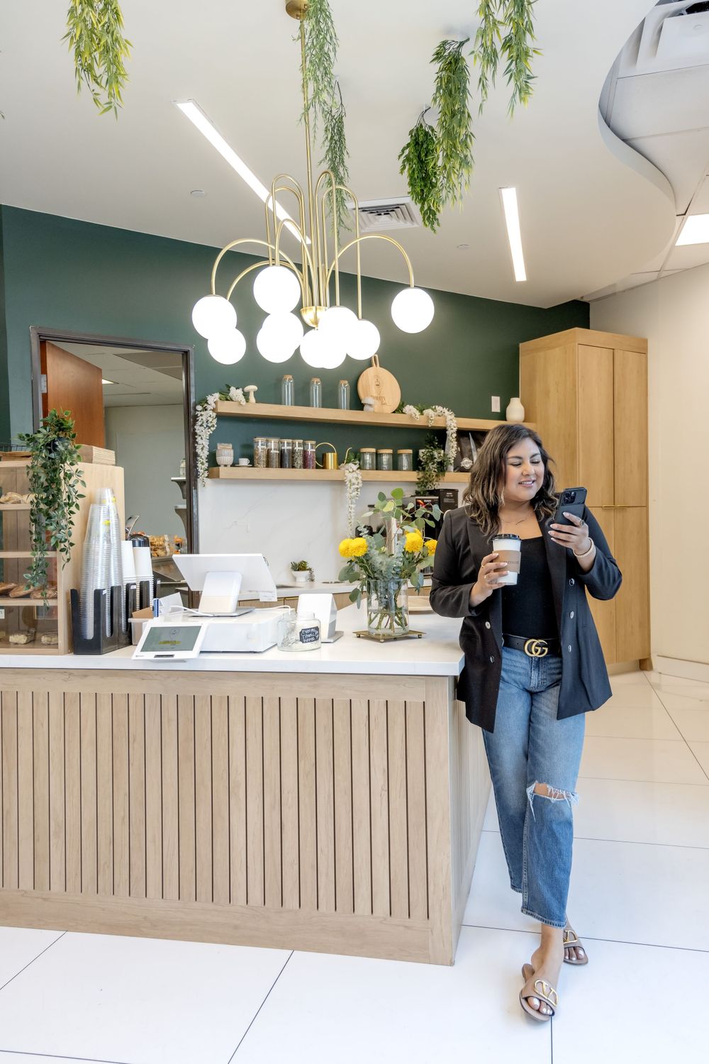 Modern cafe interior with hanging plants, green accent wall and wooden counter.