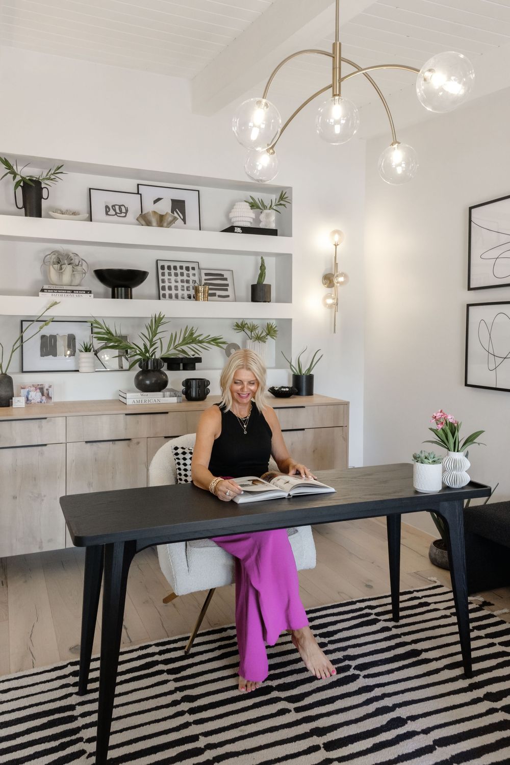 Stylish workspace with open shelving, modern lighting and black desk on striped area rug.