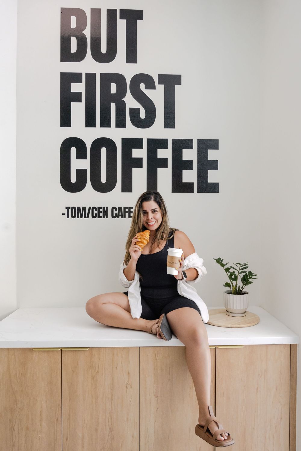 Lifestyle photo at Tom/Cen Cafe with someone sitting beneath a 'But First Coffee' wall sign.