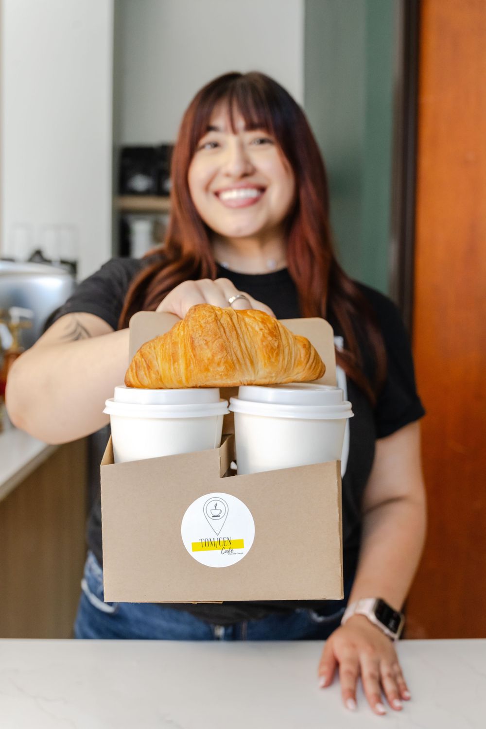 Someone holding a box with croissants and coffee cups with a bright smile.