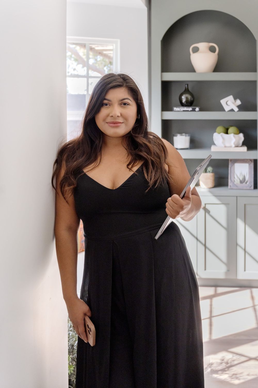 Interior lifestyle photo of someone in a black dress standing beside built-in gray shelves.