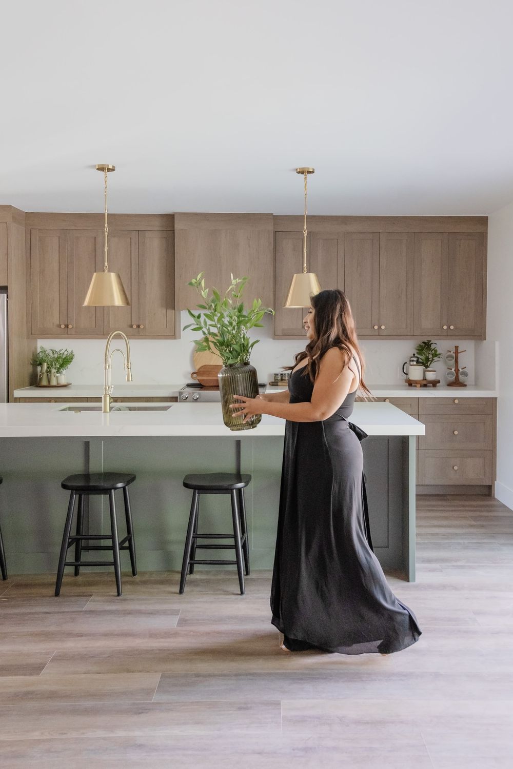 A black maxi dress on someone placing a plant vase on a modern white kitchen counter with brass pendant lights.
