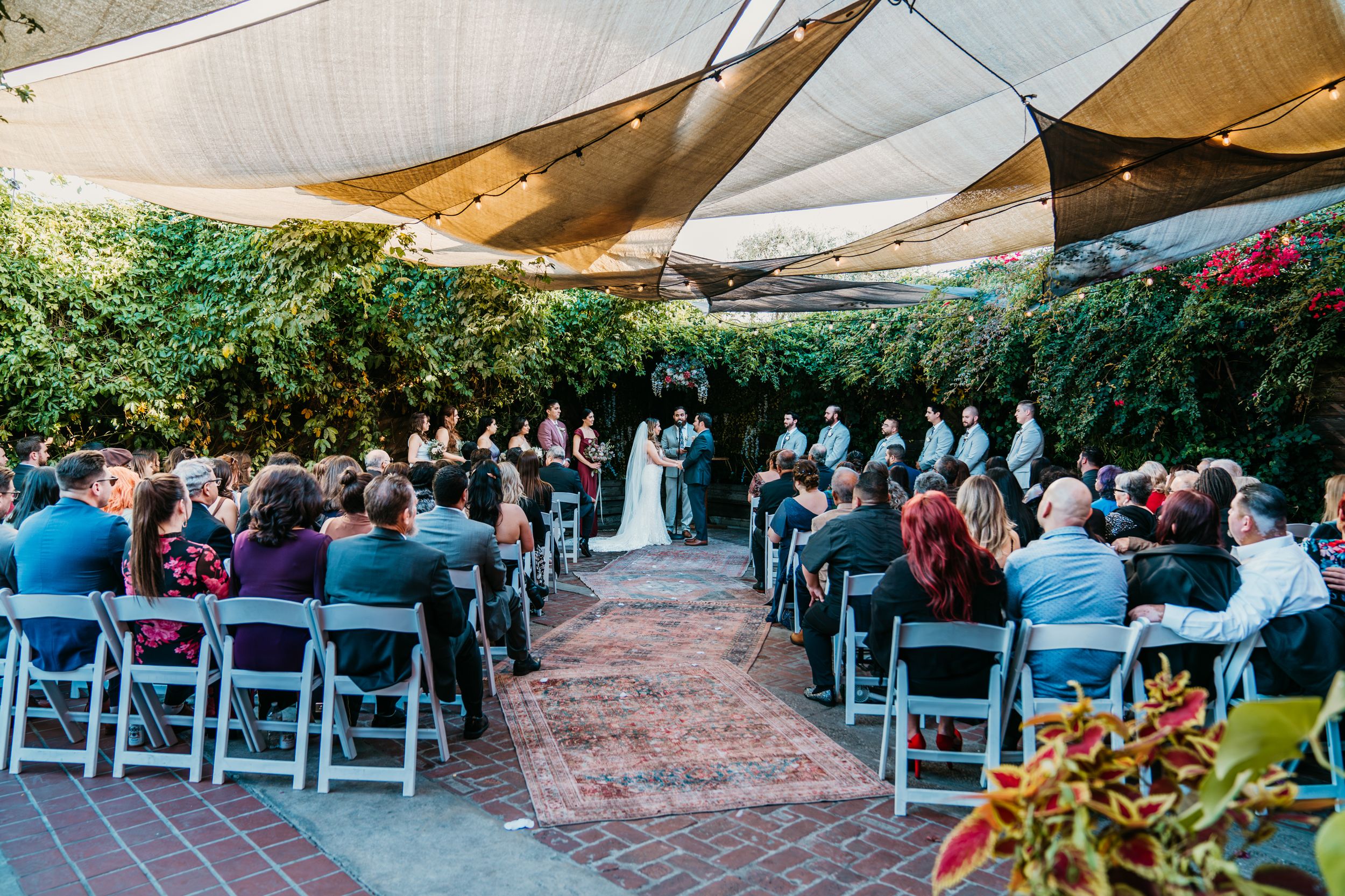 Outdoor wedding ceremony setup with white canopy and rows of chairs in a garden setting.