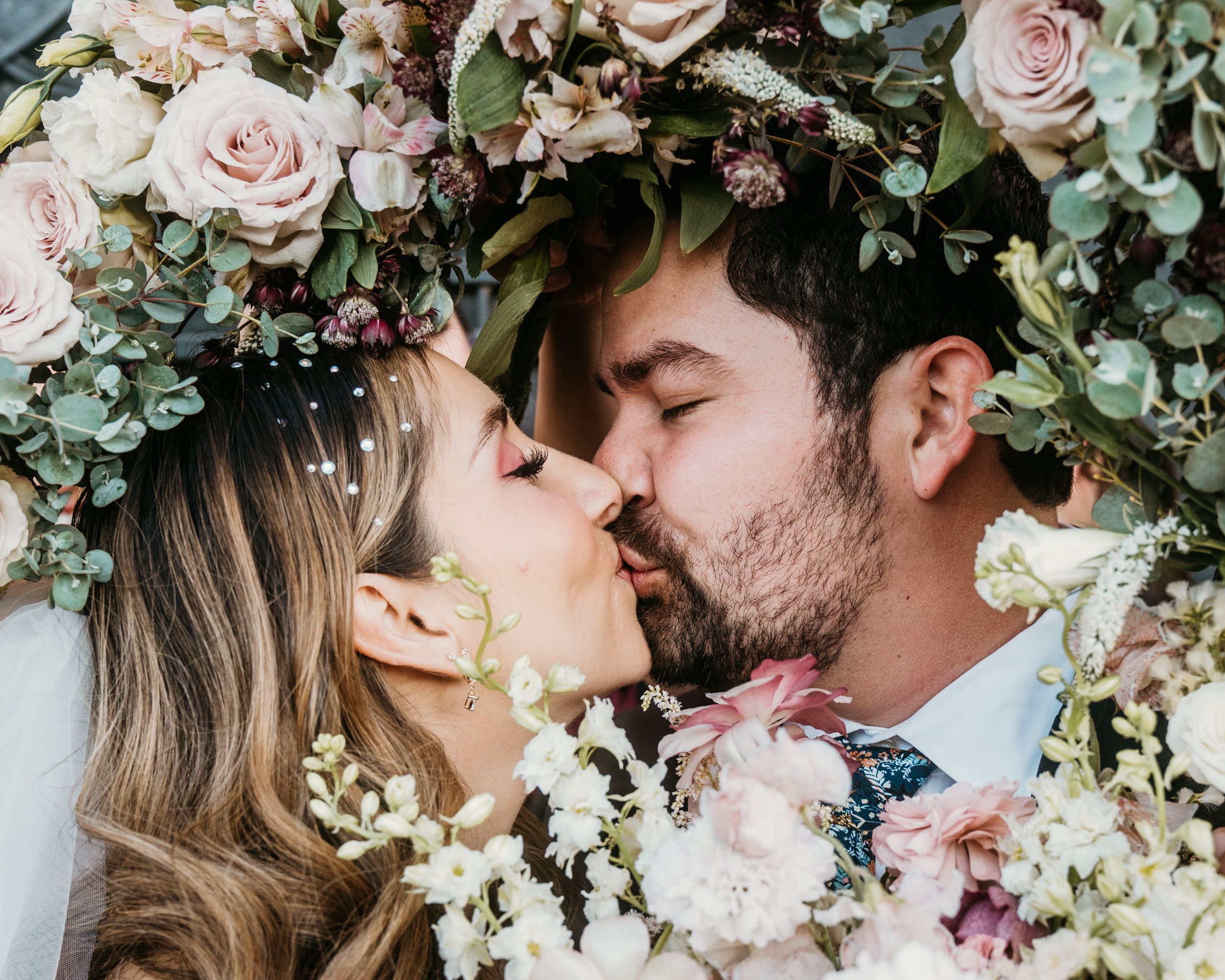 Romantic kiss framed by floral arch with roses and greenery.
