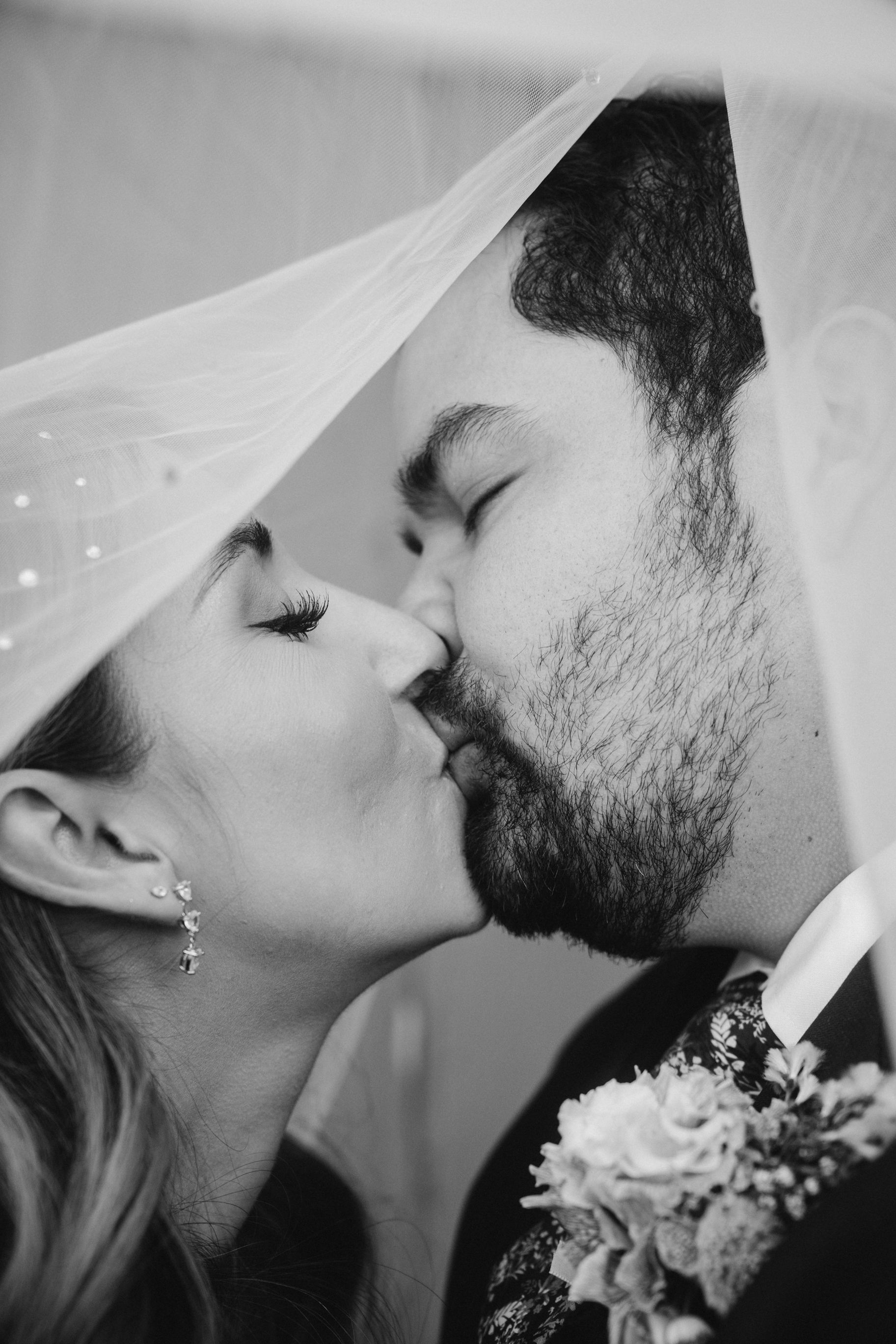 Romantic black and white photo of newlyweds sharing a tender kiss under a delicate veil.