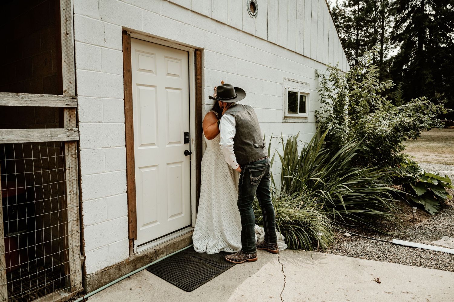Wedding couple shares private moment against white building exterior.