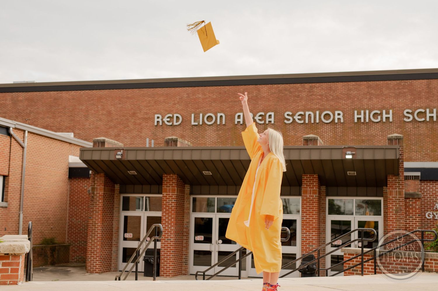 Yellow graduation cap being tossed in the air against brick school building backdrop.