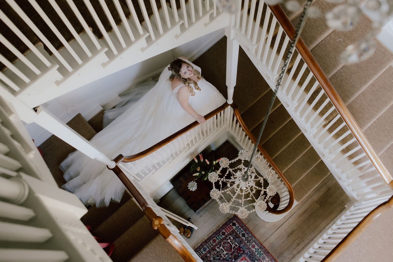 Aerial view of bride descending elegant white staircase in flowing wedding gown.
