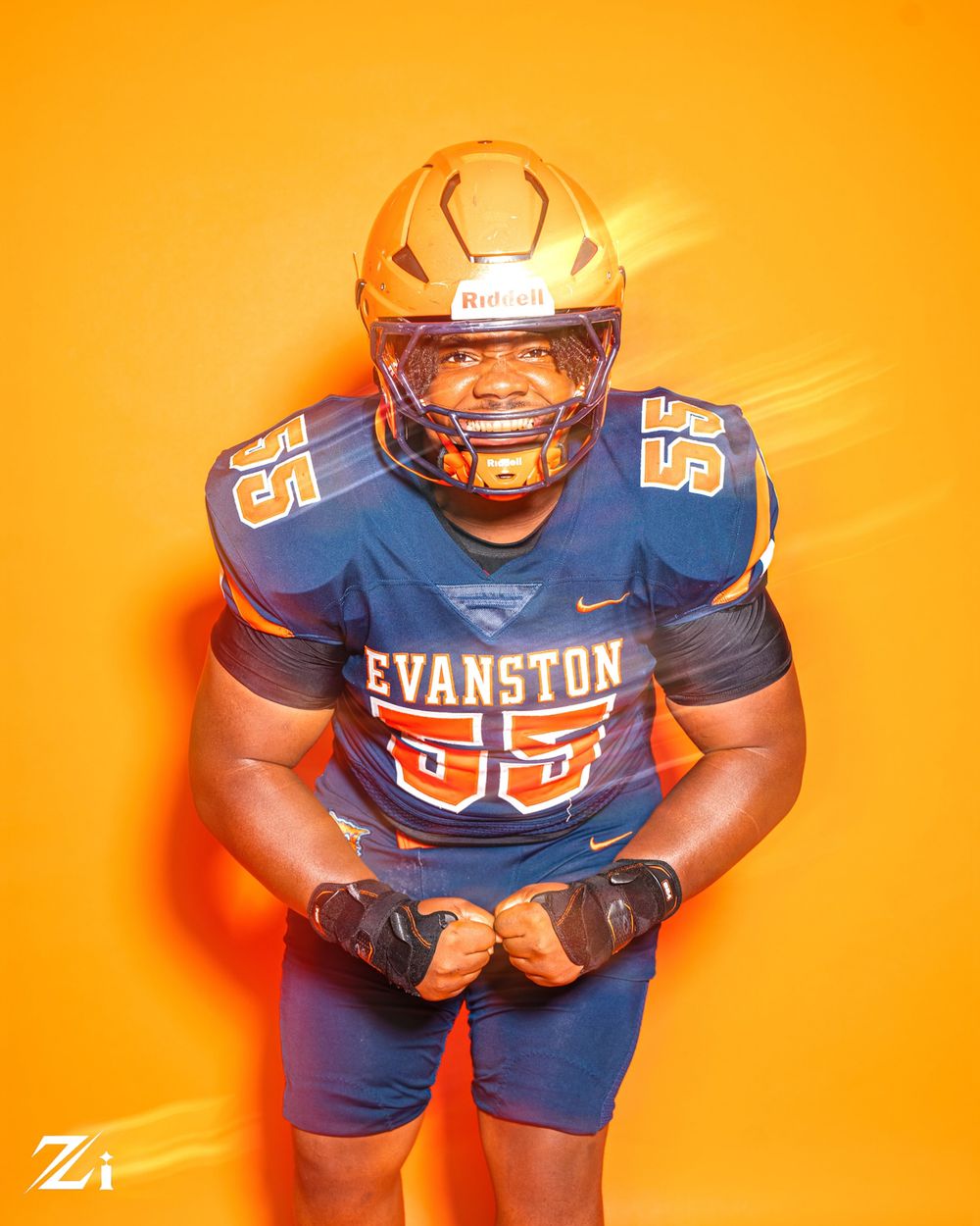 Football player wearing blue and orange Evanston uniform poses dramatically against bright orange background.