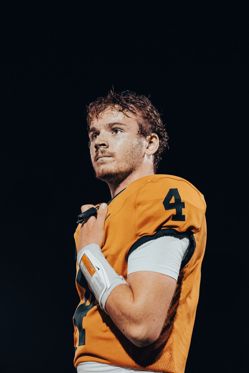 Football player in orange jersey number 4 poses dramatically against dark background.
