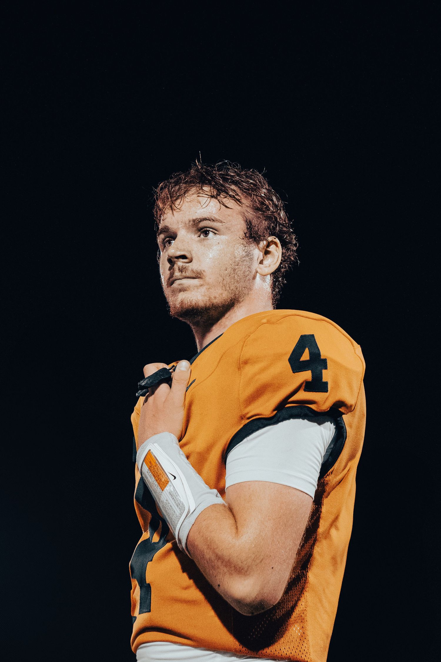 Football player in orange jersey number 4 poses dramatically against dark background.