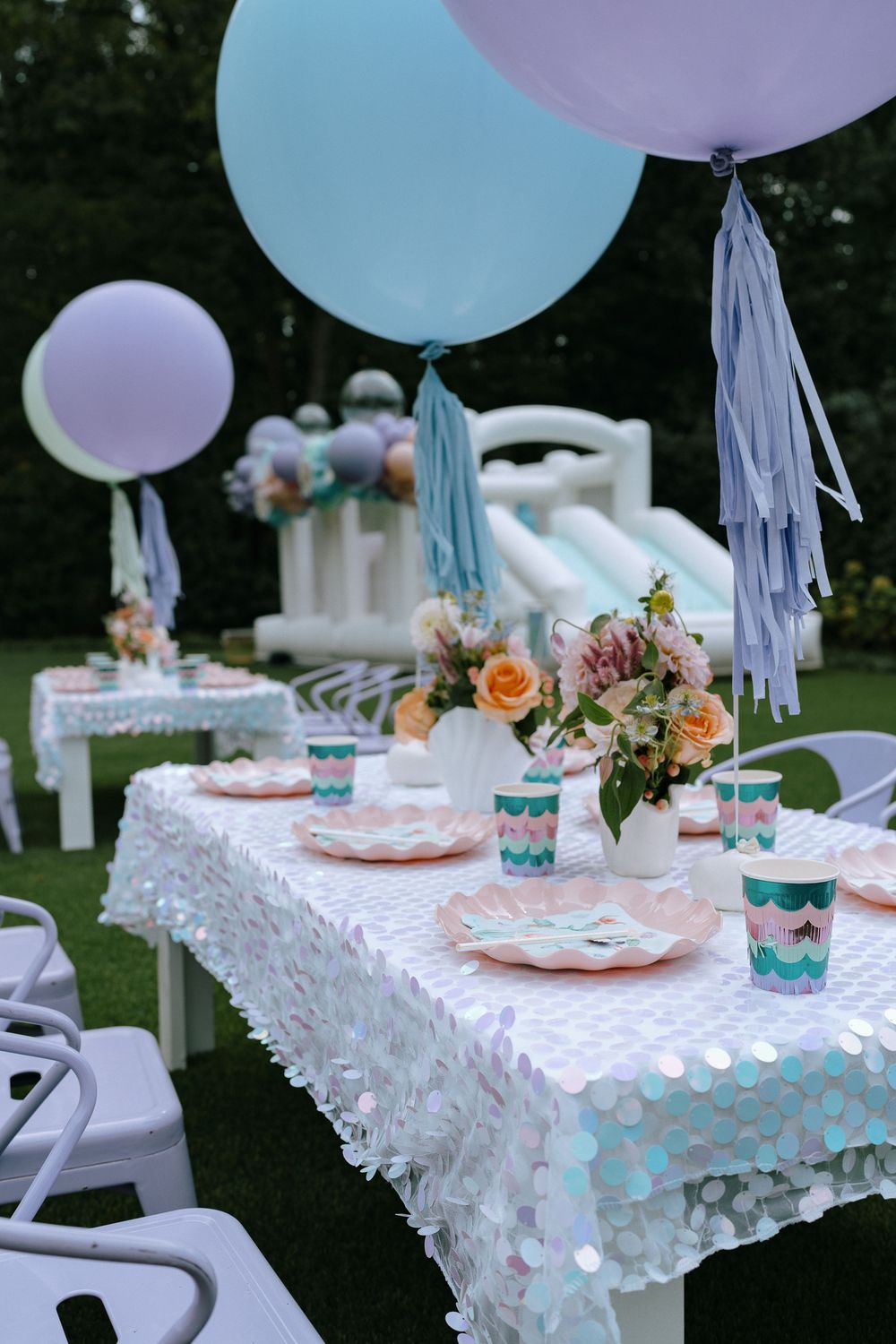Elegant outdoor birthday party table with pastel balloons, sequin tablecloth, and floral centerpiece.