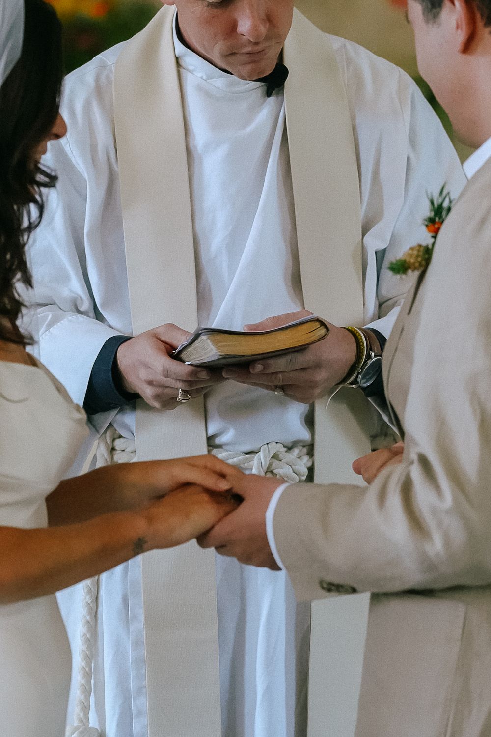 Priest reading from a book as bride and groom hold hands during a traditional wedding ceremony.