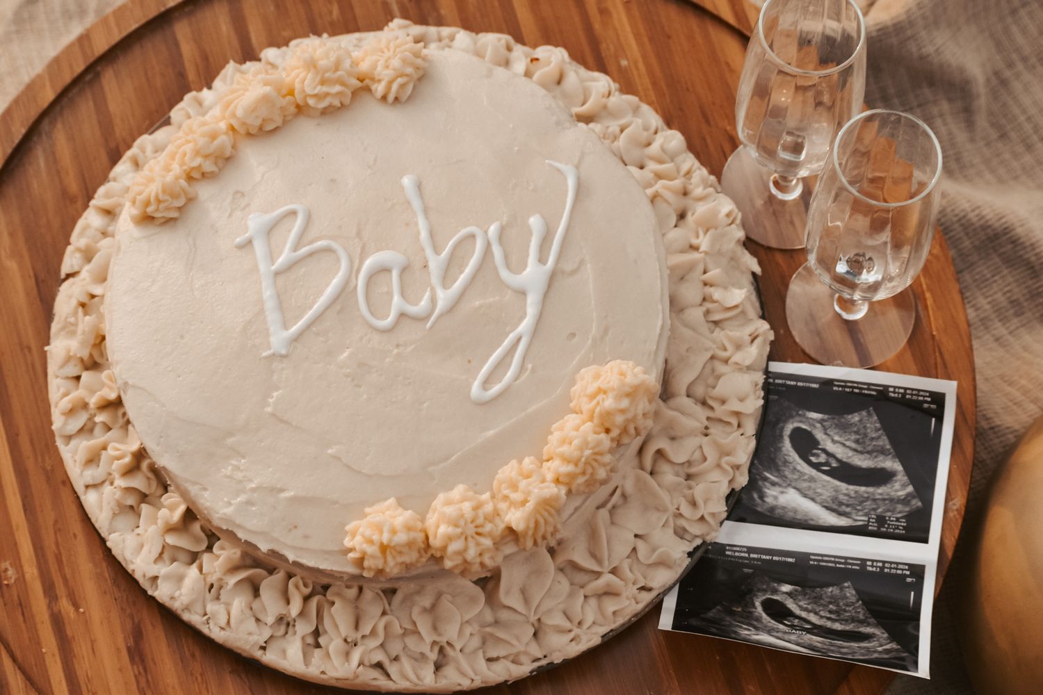 Baby celebration cake with ultrasound photos on wooden table with champagne glasses.