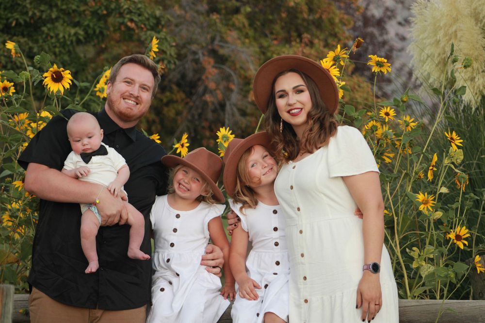 A family of five poses for a portrait with sunflowers in the background during golden hour.