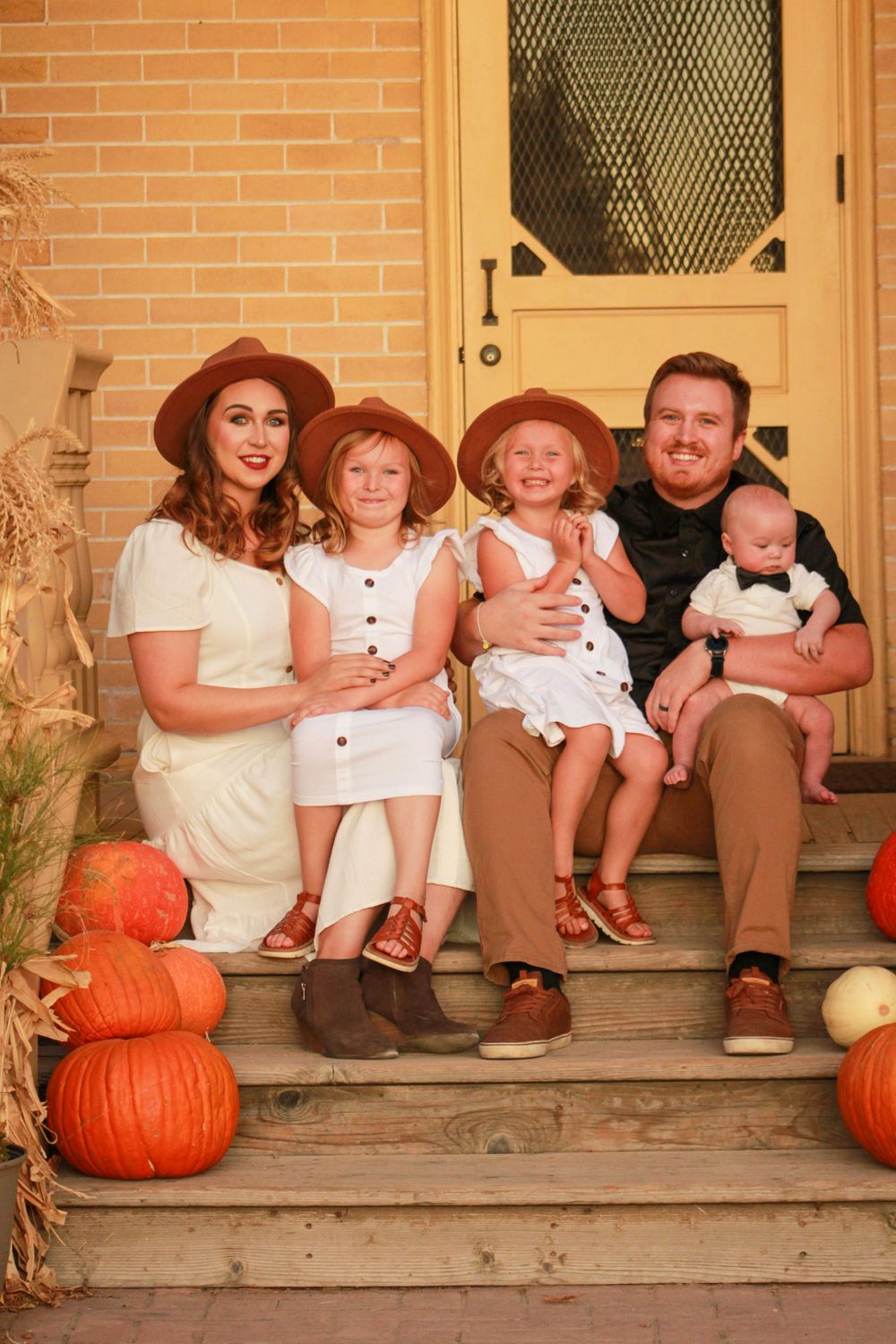 A family group sits together on rustic steps decorated with autumn pumpkins.