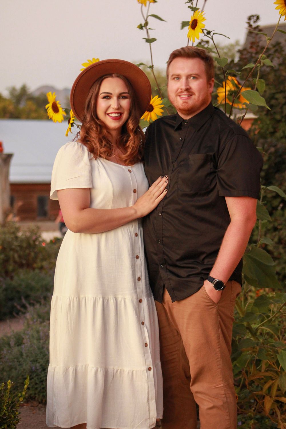 A couple poses together in front of sunflowers wearing coordinated casual outfits.