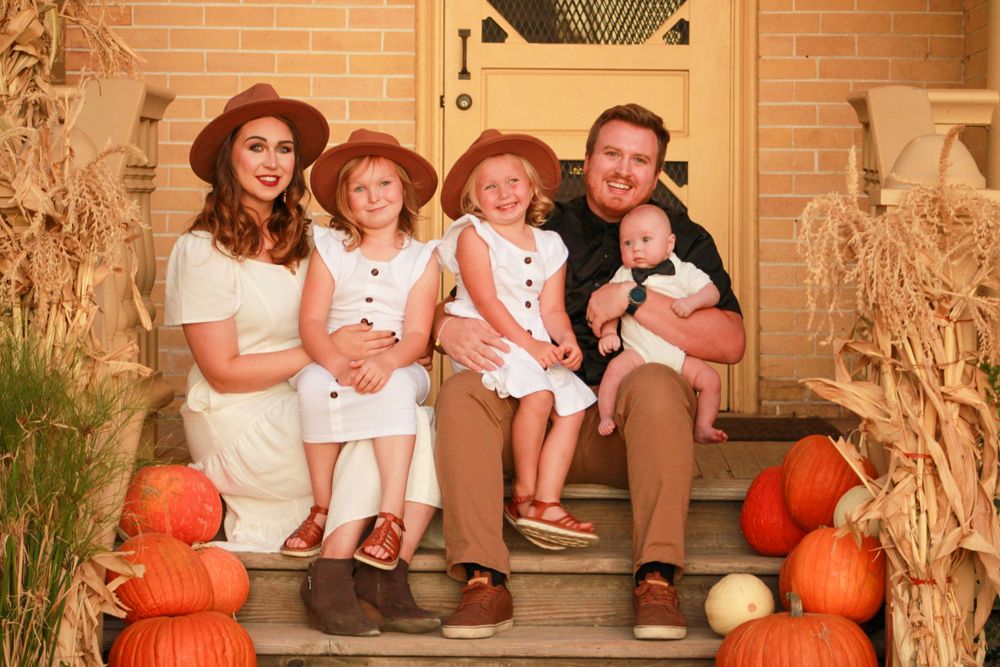 A family poses on porch steps with fall decorations and pumpkins.