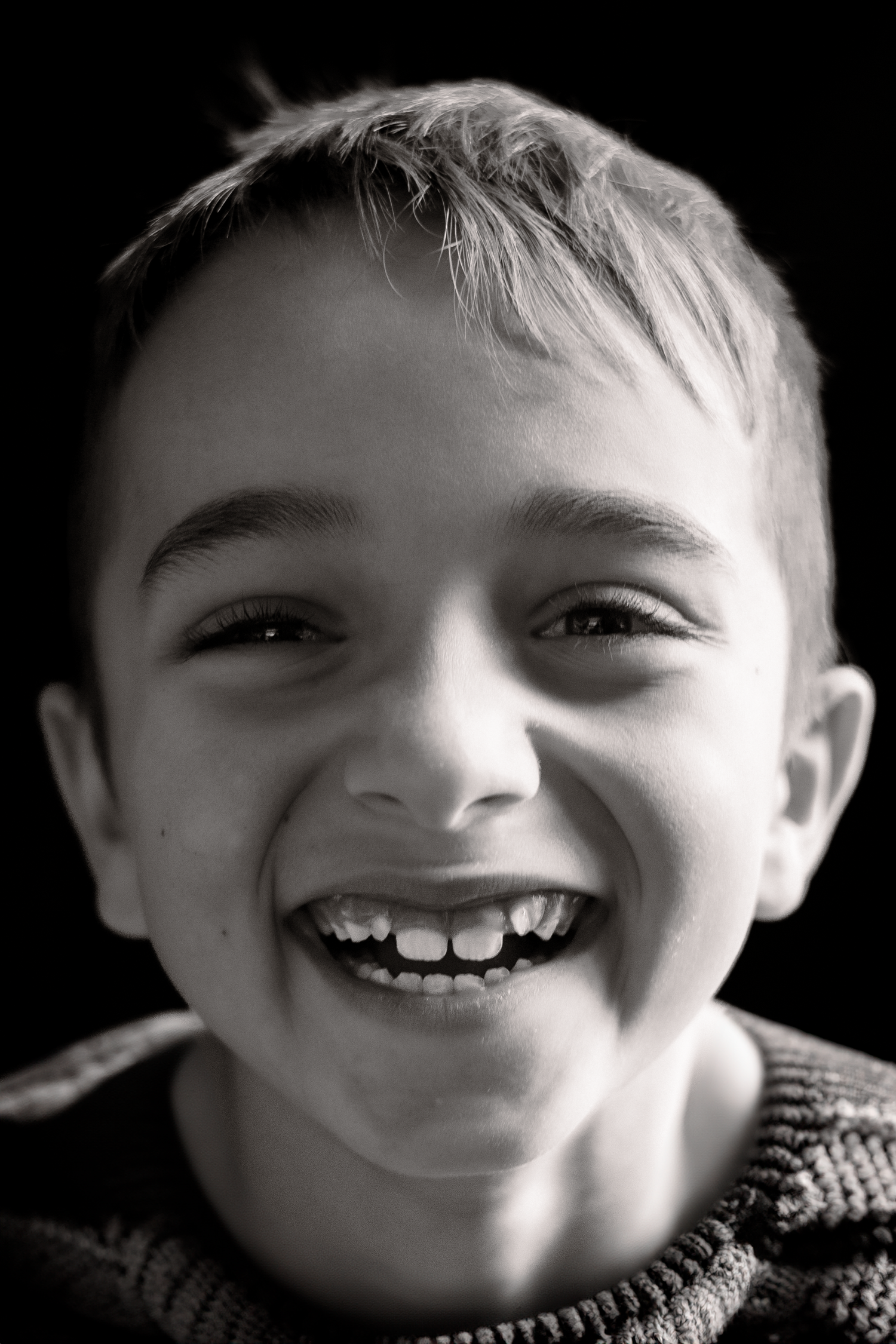 A black and white portrait of a young child with a joyful, gap-toothed smile.