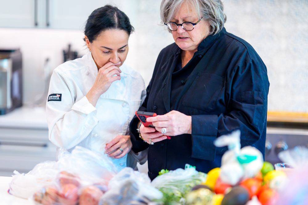 Two chefs examine ingredients together in a commercial kitchen setting.