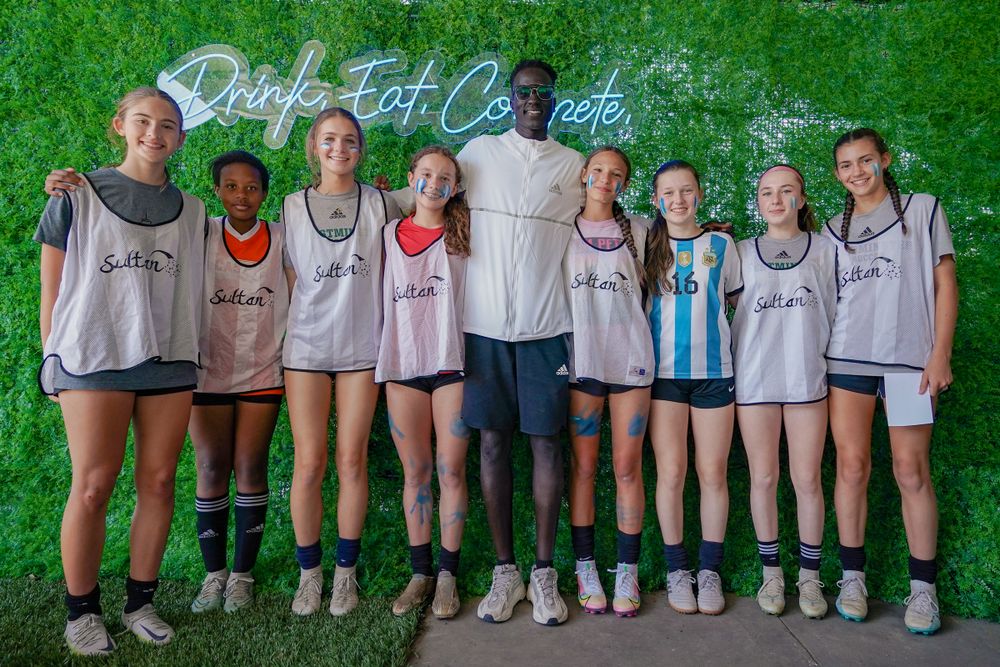 A sports team in matching jerseys poses against a green wall with text decoration.