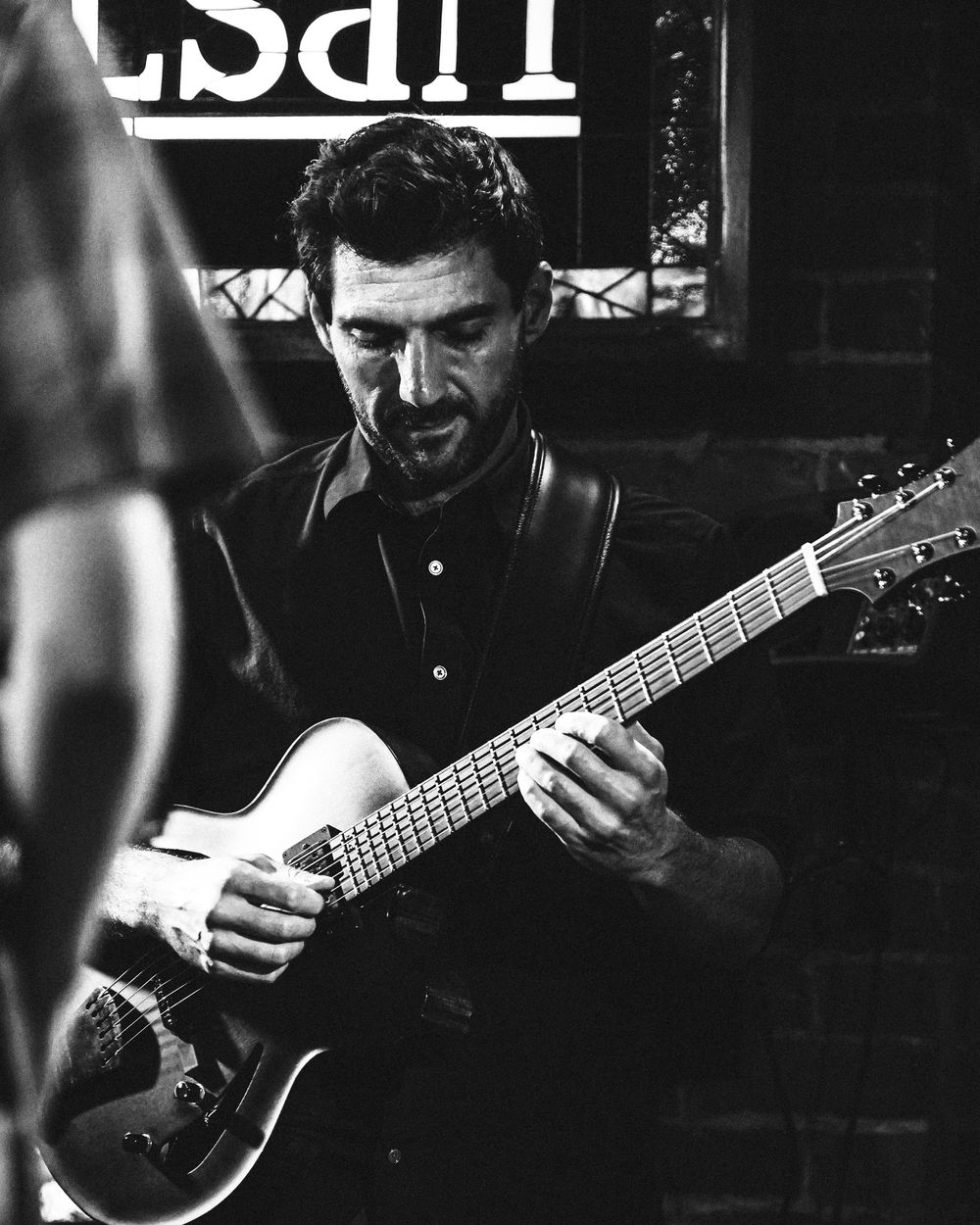 Guitarist performing in dark venue with focused expression in black and white.